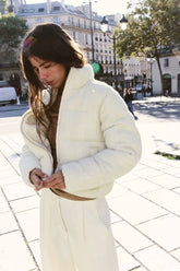 Woman wearing a white puffer jacket on a city street.